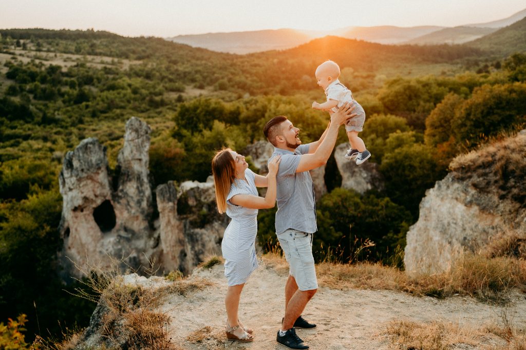 Szabadban készült családi fotó naplementében, ahol az apa felkapja a levegőbe a születésnapos gyereket, természetes és érzelmes pillanat
