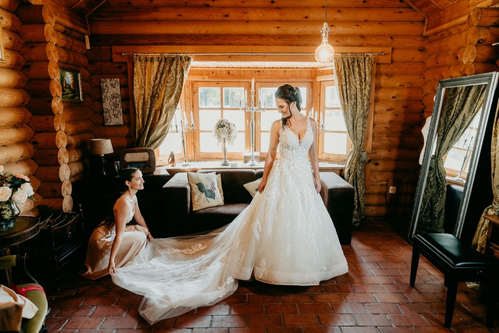 Getting ready bride on her wedding morning, makeup and dressing in soft natural window light, intimate wedding preparations with warm wood interior.
