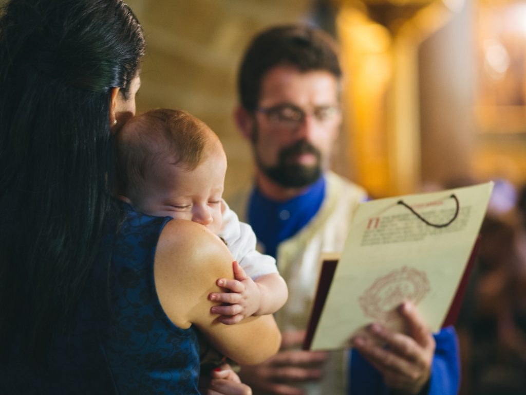 Ortodox keresztelő Cipruson, atya megáldja a babát a templomban, dokumentarista és természetes esküvői stílusban készült fénykép