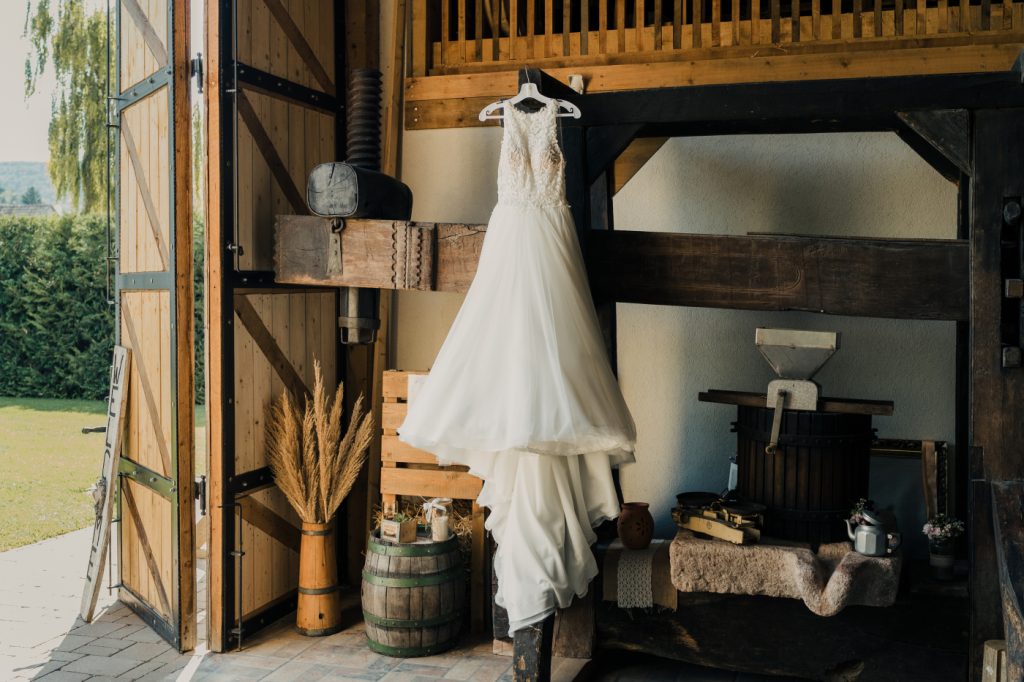 Esküvői menyasszonyi ruha felakasztva rusztikus pajta dekor mellett, vintage hangulatú pajtaesküvő helyszínen